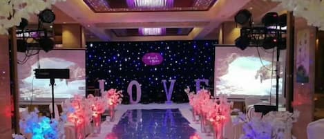 A stage with a 'LOVE' backdrop, surrounded by floral arrangements and a reflective floor.