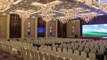 A banquet hall with rows of white chairs, a large screen, and chandeliers.