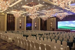 Un salón de banquetes con filas de sillas blancas, una pantalla grande y candelabros.
