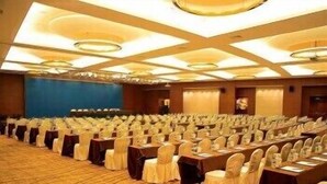 Un salón de conferencias con filas de mesas y sillas, una pared azul y suelo alfombrado.