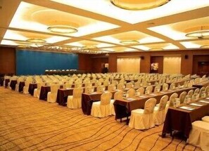 A conference room with rows of tables and chairs, a blue wall, and a carpeted floor. - Fortune Bond Hotel (Ningbo)