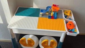 Una mesa de juegos LEGO con cuatro secciones, cada una de diferente color, y dos compartimentos de almacenamiento debajo.
