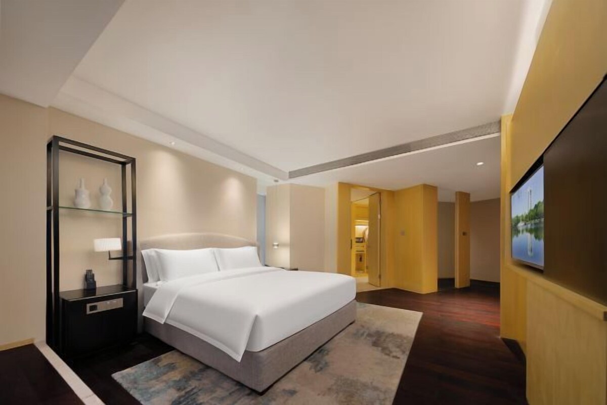 A hotel room with a large bed, a nightstand, a glass display cabinet, and a television on the wall.