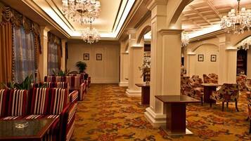 A hotel lobby with striped sofas, a patterned carpet, chandeliers, and a dining area with floral chairs.