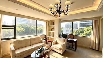 A spacious living room with a sofa, armchair, and coffee table, large windows with a city view, and a chandelier.