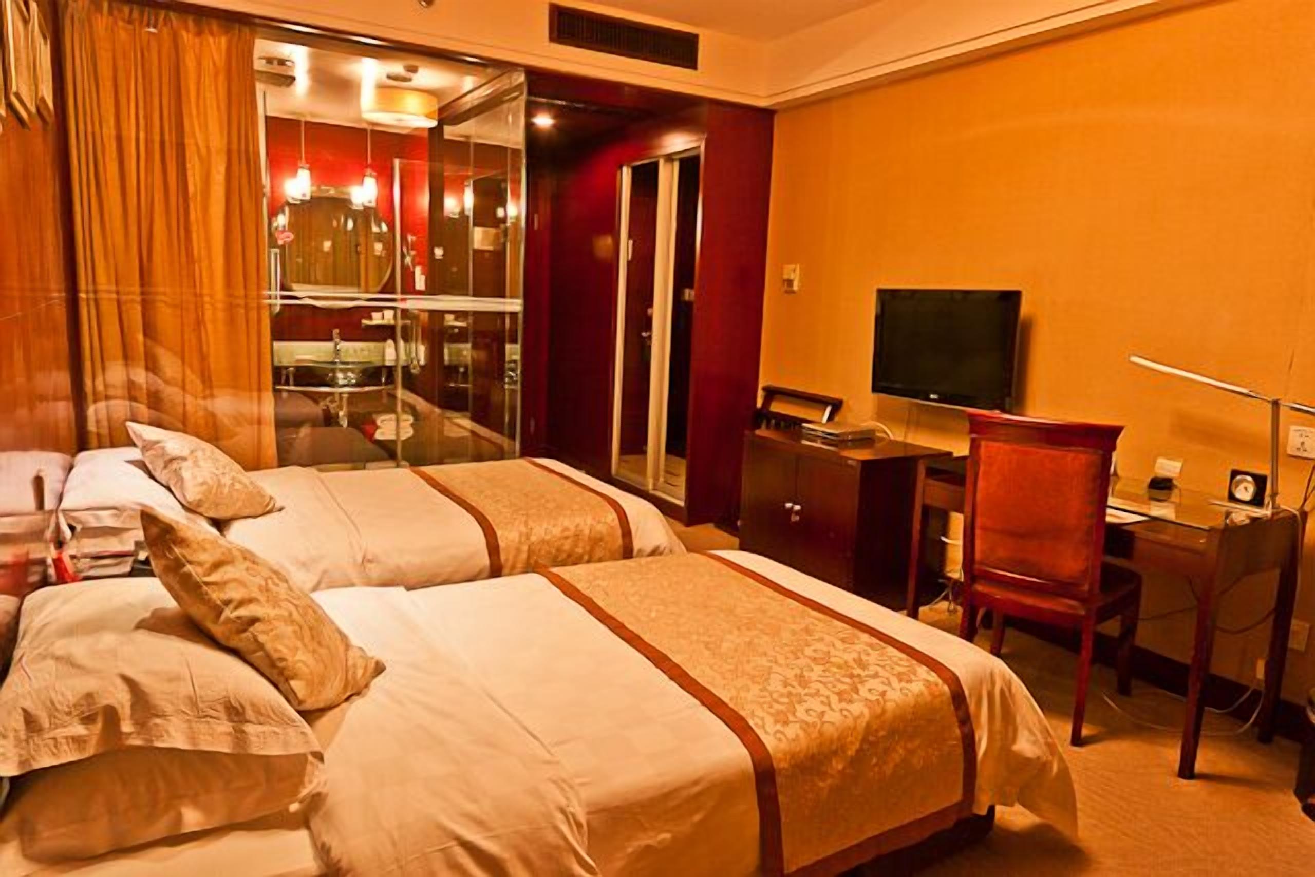 Habitación de hotel con dos camas, un escritorio, una silla, un televisor y un espejo.