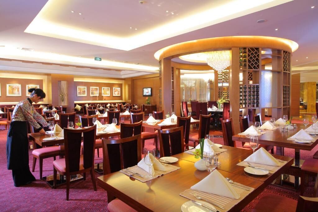 Une salle à manger d’hôtel avec de nombreuses tables dressées pour les clients, une colonne décorative centrale et un écran de télévision fixé au mur.