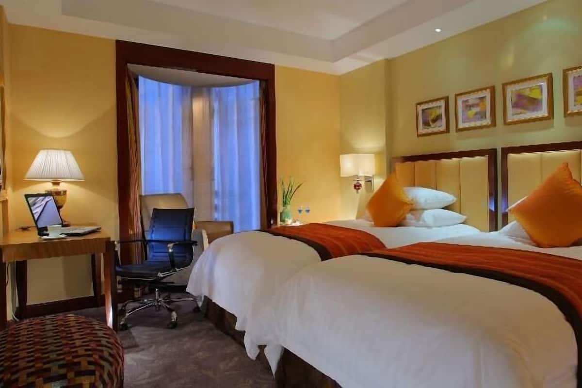 Habitación de hotel con dos camas, un escritorio, una computadora portátil, una silla y una mesita de noche con una lámpara.