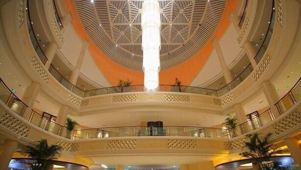 Een meerlaags atrium met een open centrale ruimte, glazen balustrades en decoratieve plafondpatronen.