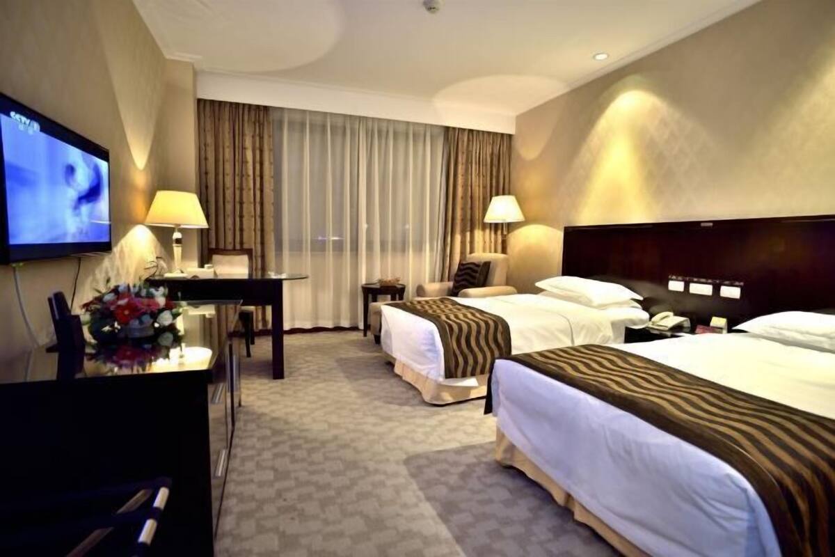 A hotel room with a TV, two beds, a desk, and a chair.