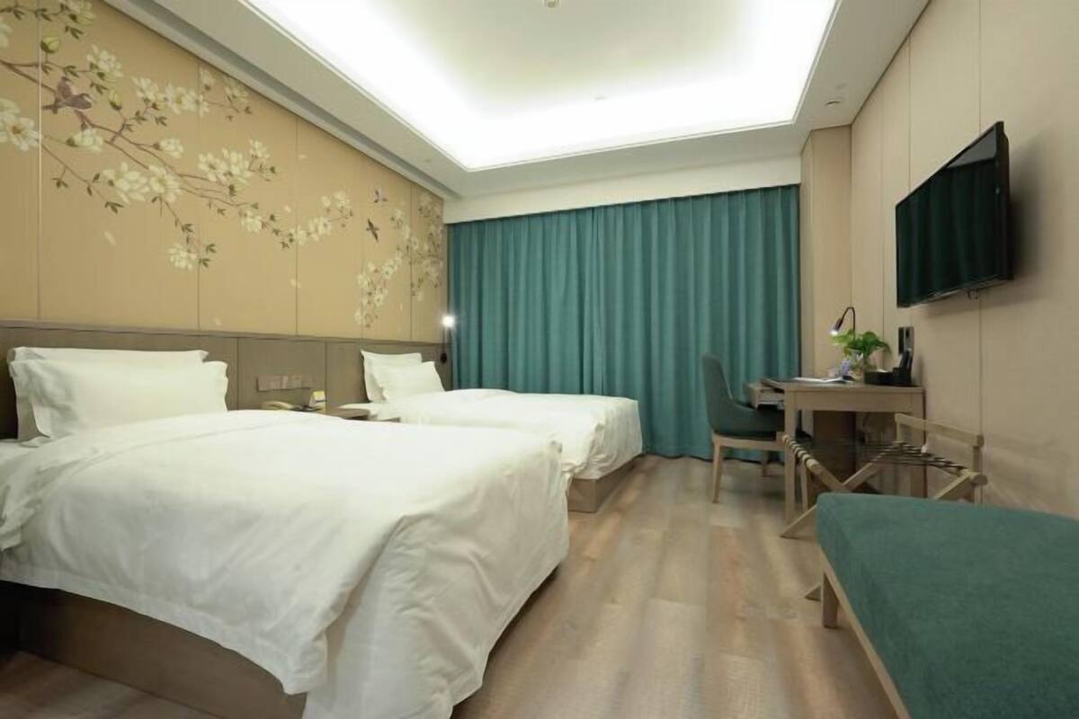 A hotel room with two beds, a desk, a chair, a TV, and a window with curtains.