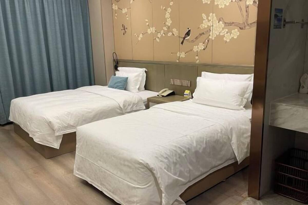Two single beds with white linens, a wooden headboard, a telephone, and a wall with a floral pattern.