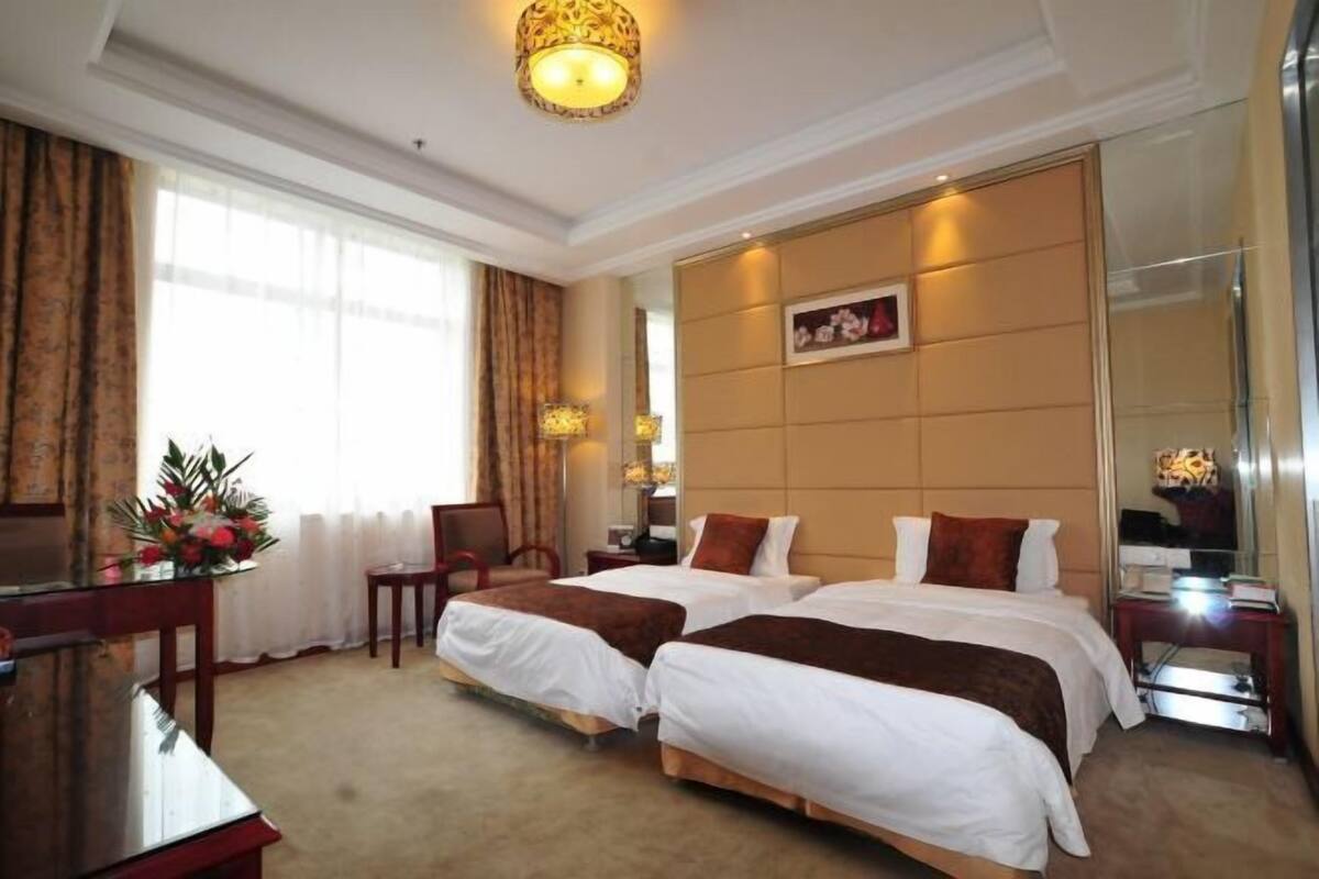 A hotel room with two beds, a desk, a chair, a mirror, and a large window.