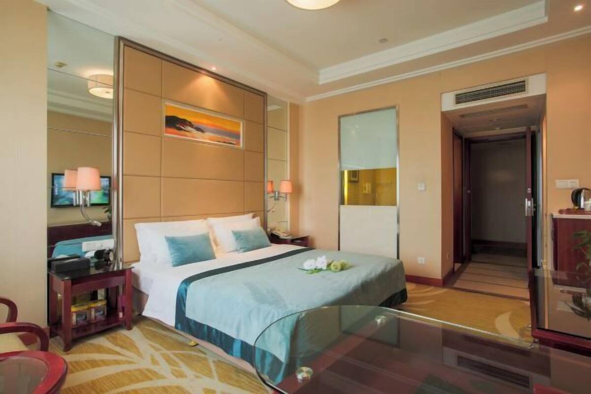 A hotel room with a bed, bedside tables, a TV, a mirror, and a door leading to a hallway.