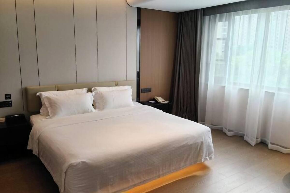 A hotel room with a large bed, a nightstand, a telephone, and a window with curtains.