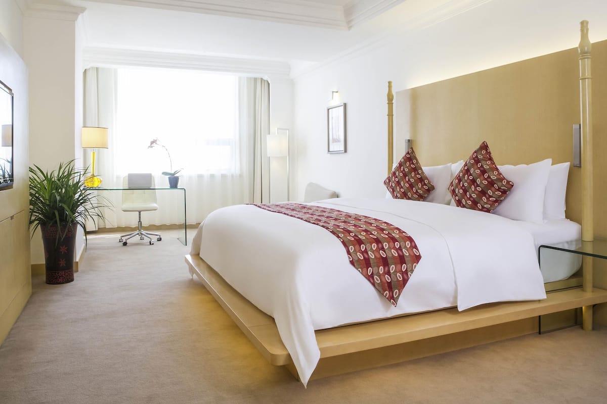 A hotel room with a large bed, bedside tables, a desk, and a potted plant.