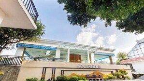 A modern building with a glass facade, a sign with Chinese characters, and a landscaped area with shrubs and a small fountain. - Liuzhou Hotel (Liuzhou)