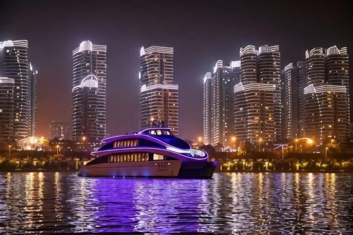 Un grand yacht illuminé, voguant sur une eau calme, avec la silhouette d’une ville en arrière-plan.