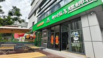 Un edificio con letrero verde, mesas al aire libre y una ventana con el rótulo de café.