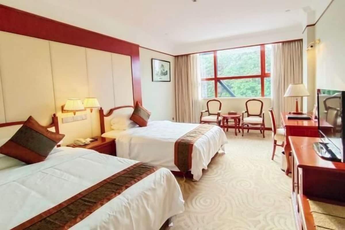 Une chambre d’hôtel avec deux lits, un bureau, une chaise, une télévision et une fenêtre avec des rideaux.