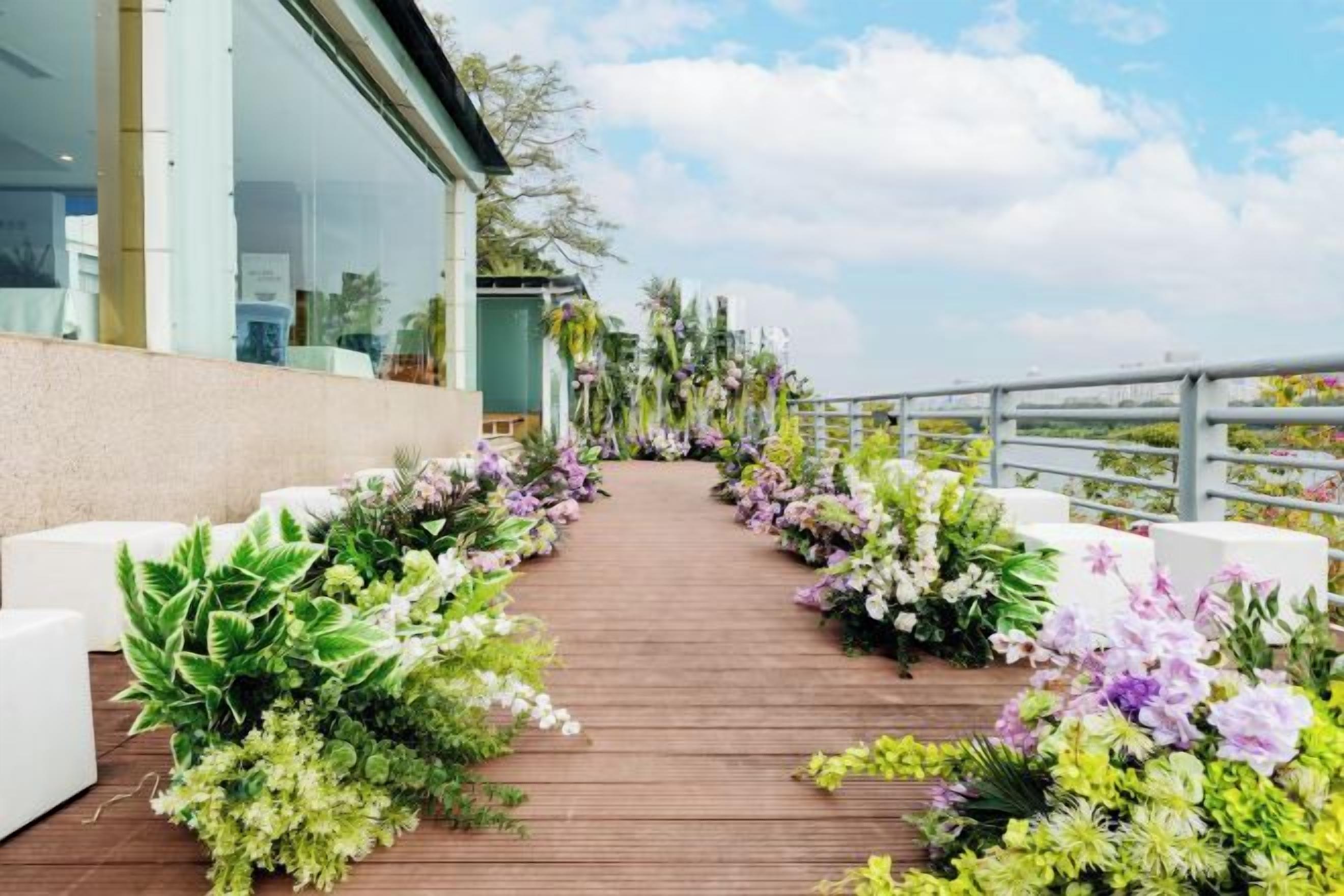 Una terraza de madera con un arreglo floral en un lado y un edificio en el otro.