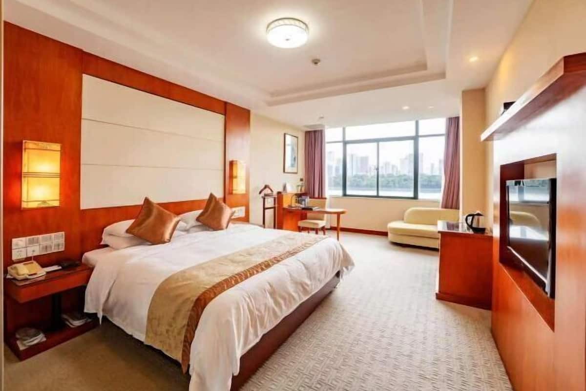 Une chambre d’hôtel avec un grand lit, un bureau, une chaise, une télévision et une fenêtre donnant sur la ville.