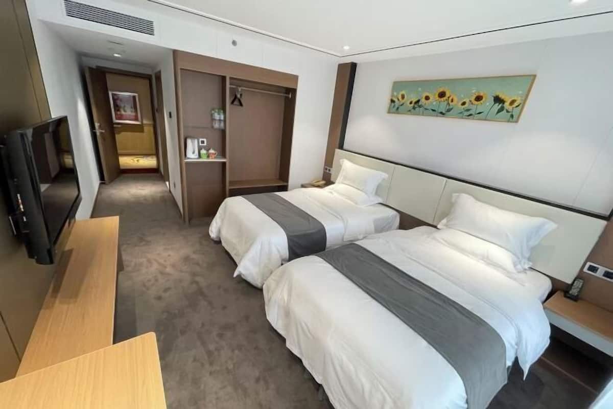A hotel room with two beds, a TV, a desk, a wardrobe, and a painting on the wall.