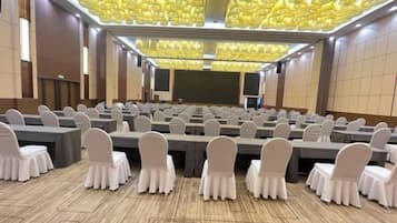 A conference room with rows of tables and chairs, a large screen, and a patterned ceiling.