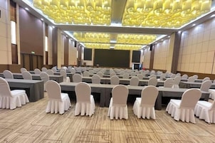 Un salón de conferencias con mesas y sillas dispuestas en filas, una pantalla grande y un techo con diseño.