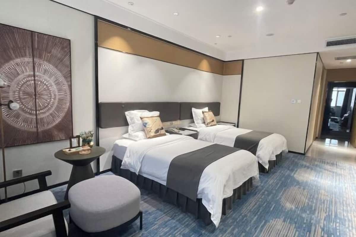 A hotel room with two beds, a small round table, a bench, and a large abstract painting on the wall.
