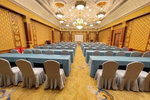 Un salón de conferencias con filas de mesas y sillas, una araña y una pizarra.
