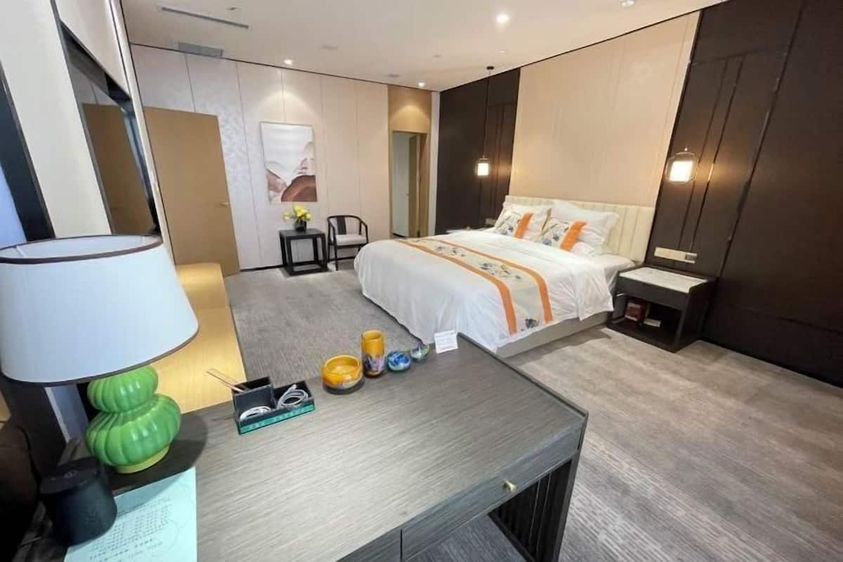 A modern hotel room with a bed, bedside table, lamp, and a small desk with a chair.