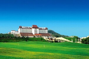 Ein großes Hotel mit mehreren Etagen und einem roten Dach, gelegen auf einem grünen Hügel unter blauem Himmel.