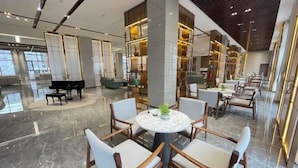 Eine moderne Hotellobby mit Marmorboden, runden Tischen und Stühlen, einem Flügel und einem großen Bücherregal.