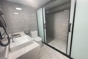 Un baño moderno con lavamanos blanco, inodoro y cabina de ducha con mampara de vidrio.