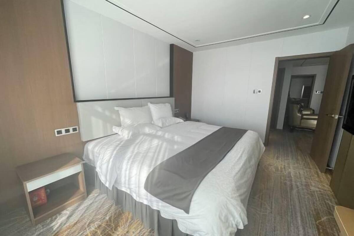 A modern hotel room with a large bed, a bedside table, a wardrobe, and a mirror.