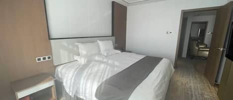 A modern hotel room with a large bed, a bedside table, a wardrobe, and a mirror.