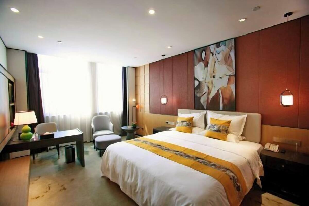 A hotel room with a bed, a desk, a chair, a lamp, and a painting on the wall.