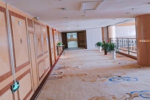 Pasillo de hotel con alfombra estampada, puertas y plantas en macetas.