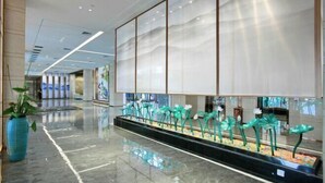 Eine moderne Lobby mit einem spiegelnden Boden, einer blauen Vase mit Pflanzen und einer Reihe grüner Dekorationsobjekte.