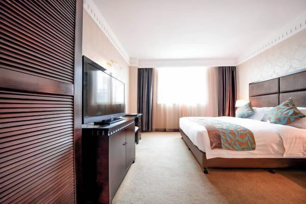 Habitación de hotel con cama, televisión, cómoda y ventana con cortinas.