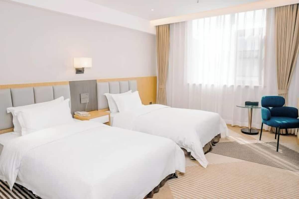 Una habitación de hotel con dos camas, una mesita de noche, una lámpara, una silla y una ventana con cortinas.