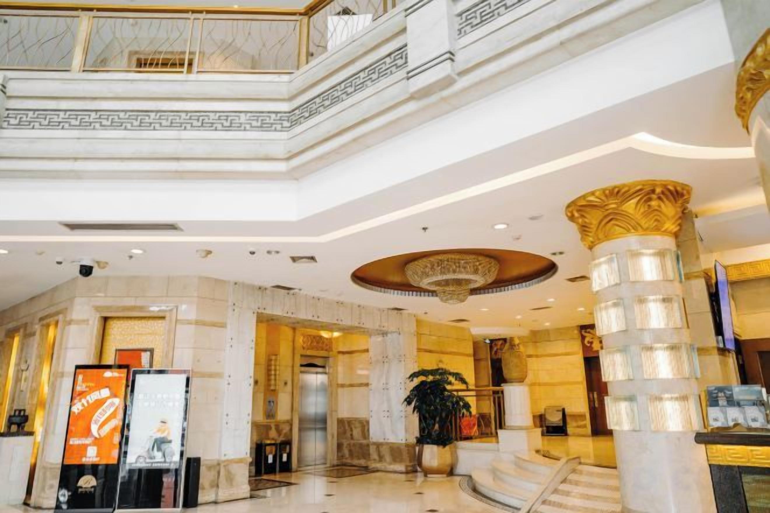 A hotel lobby with marble columns, a grand staircase, and a modern chandelier.