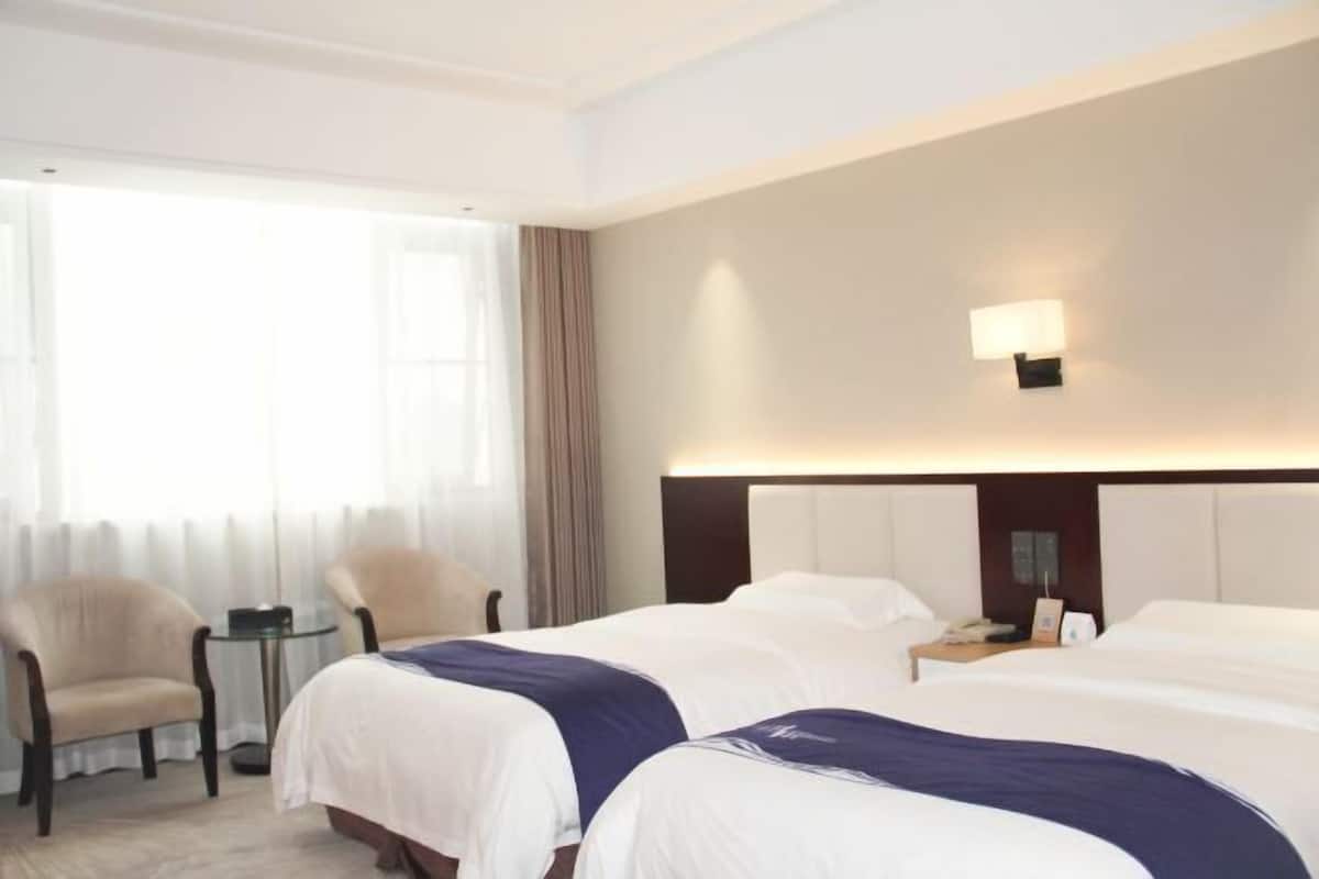 Habitación de hotel con dos camas, una silla, una mesita y una mesita de noche.