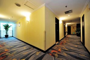 A hotel corridor with carpeted flooring, doors on both sides, and a potted plant in the center. - Regal Hotel (Guiyang)