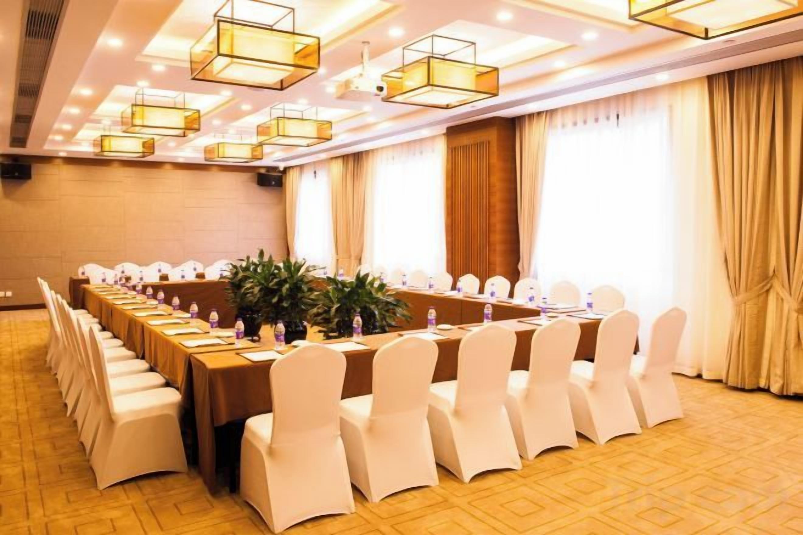 A conference room with a long table, white chairs, and pendant lighting.
