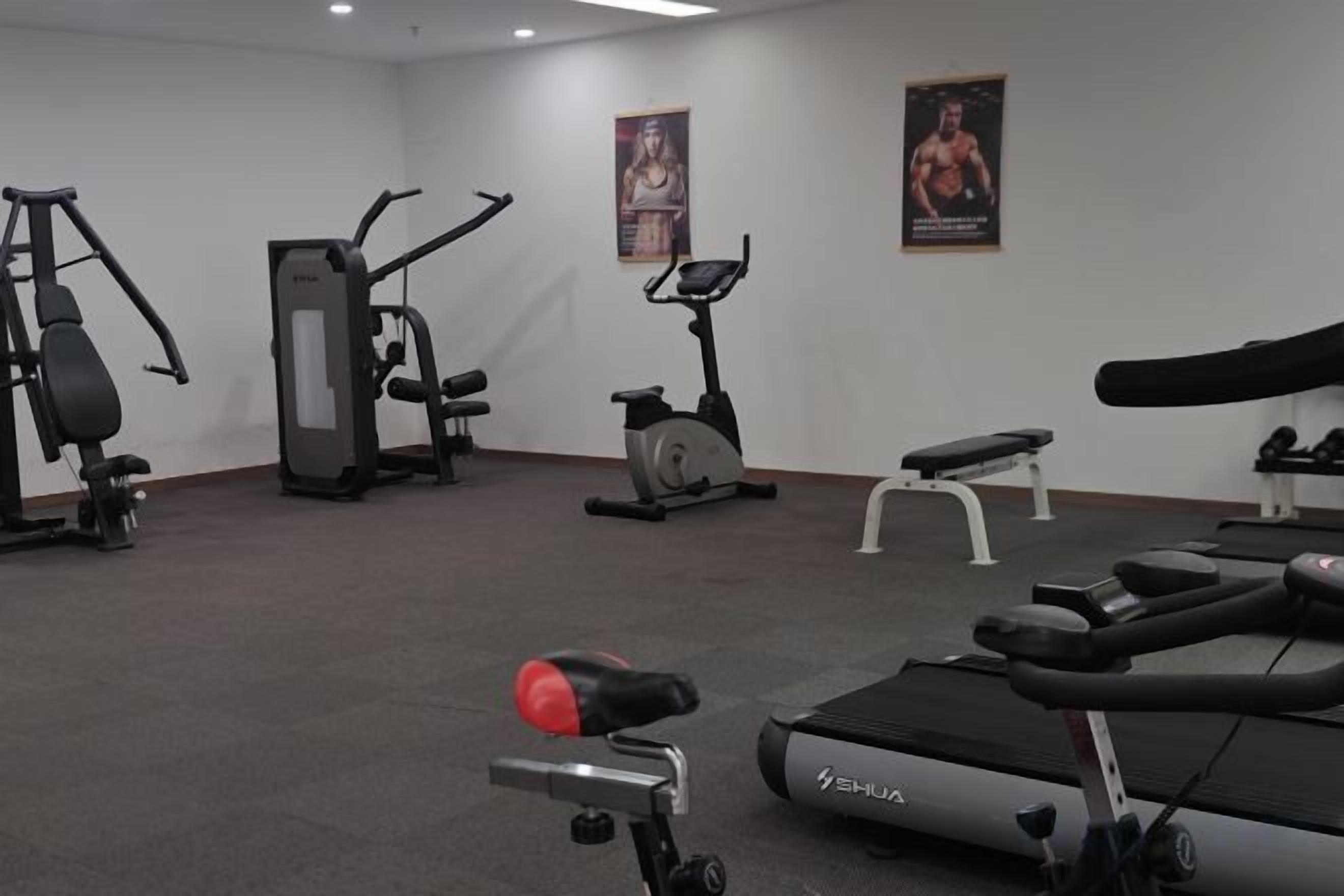Un gimnasio con diferentes equipos de ejercicio, incluyendo una cinta de correr, bicicletas estáticas y máquinas de pesas.