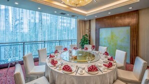 A round dining table with white chairs, a chandelier, and a large window with a view. - Regal Hotel (Guiyang)