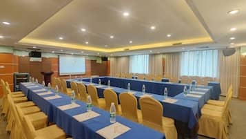 A conference room with long tables, chairs, and a projector screen.