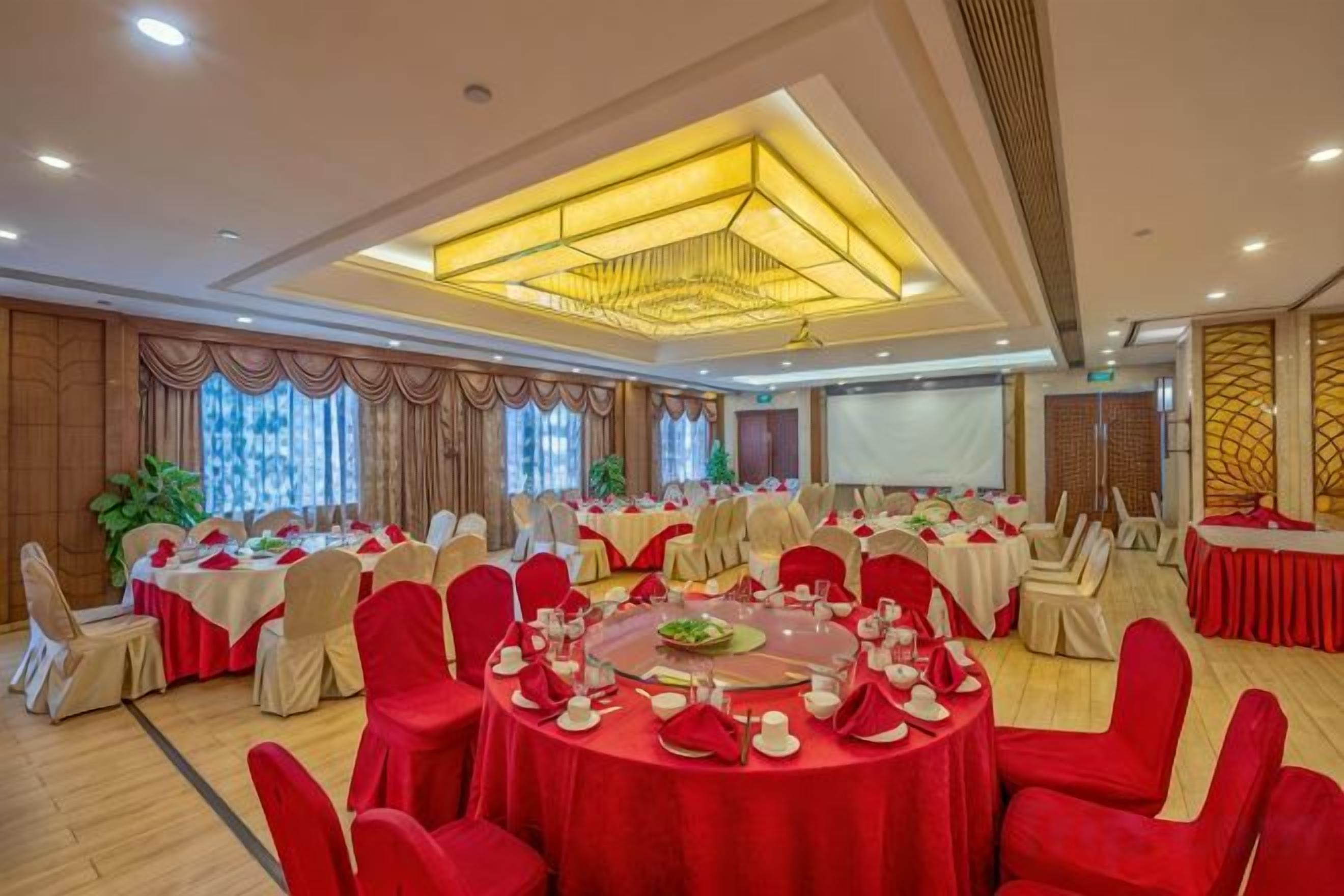 A banquet hall with round tables, red chairs, and a large screen.